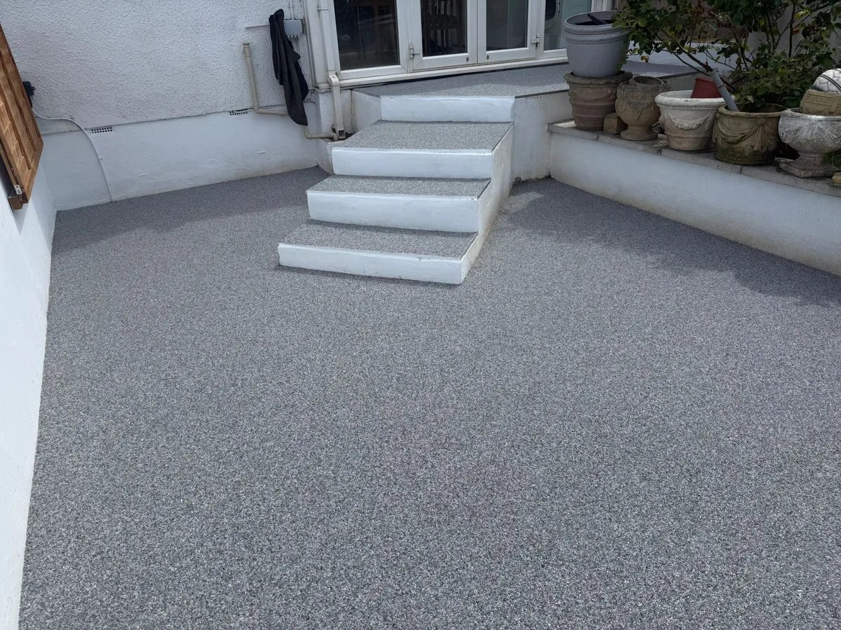 Charcoal grey resin bound patio with steps at a white rendered home - showing the long-term finish quality of a UV-stable resin system