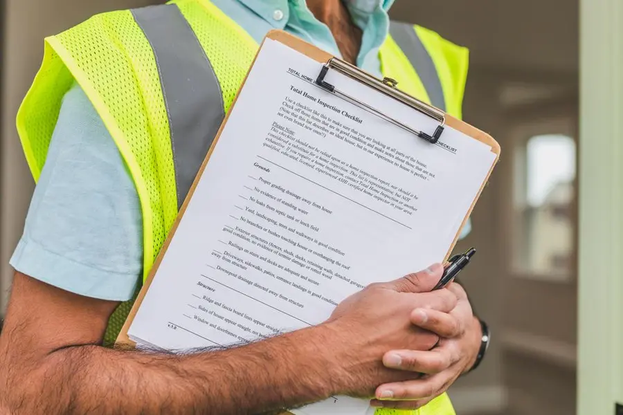 A tradesperson with a checklist reviewing a property - a thorough site assessment before quoting is a basic indicator of a serious installer