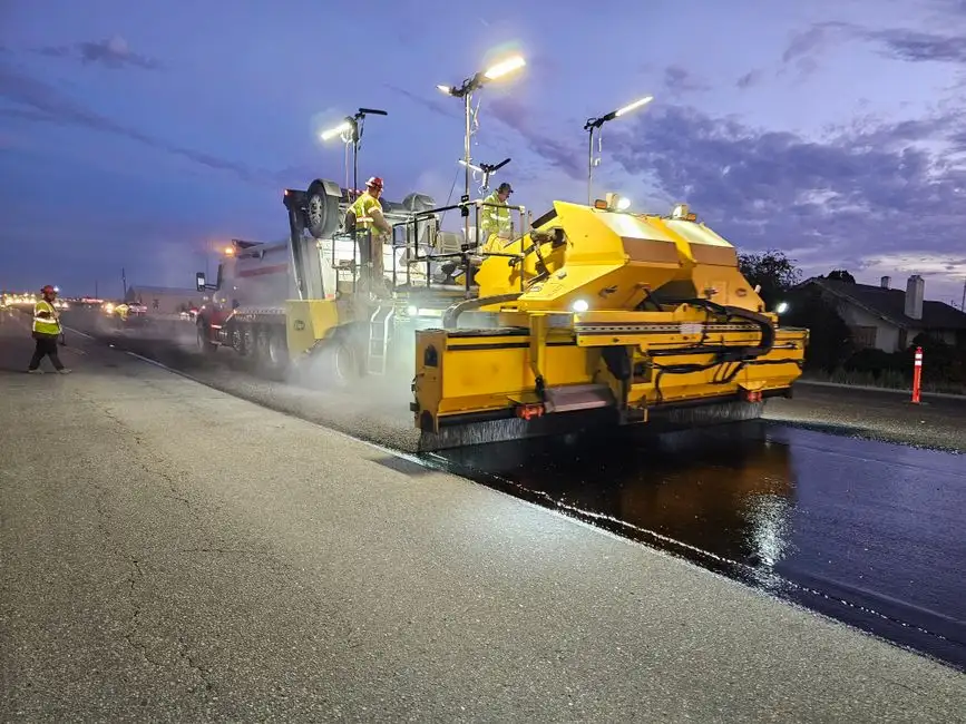 Tarmac being laid by a road surfacing machine - the machine-applied process is quicker than hand-trowelled resin and contributes to the lower upfront cost